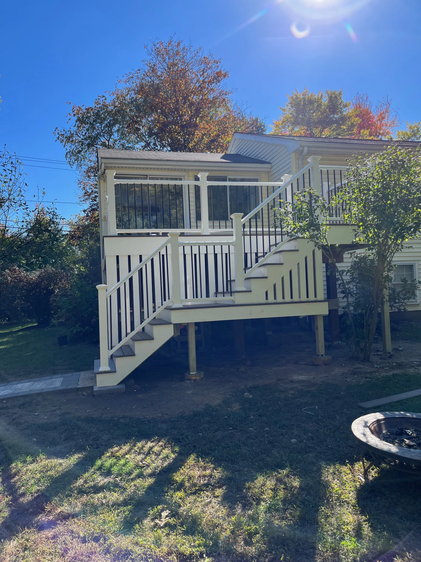 Elevated white porch with stairs, surrounded by trees and lawn, under a clear blue sky with sunlight.