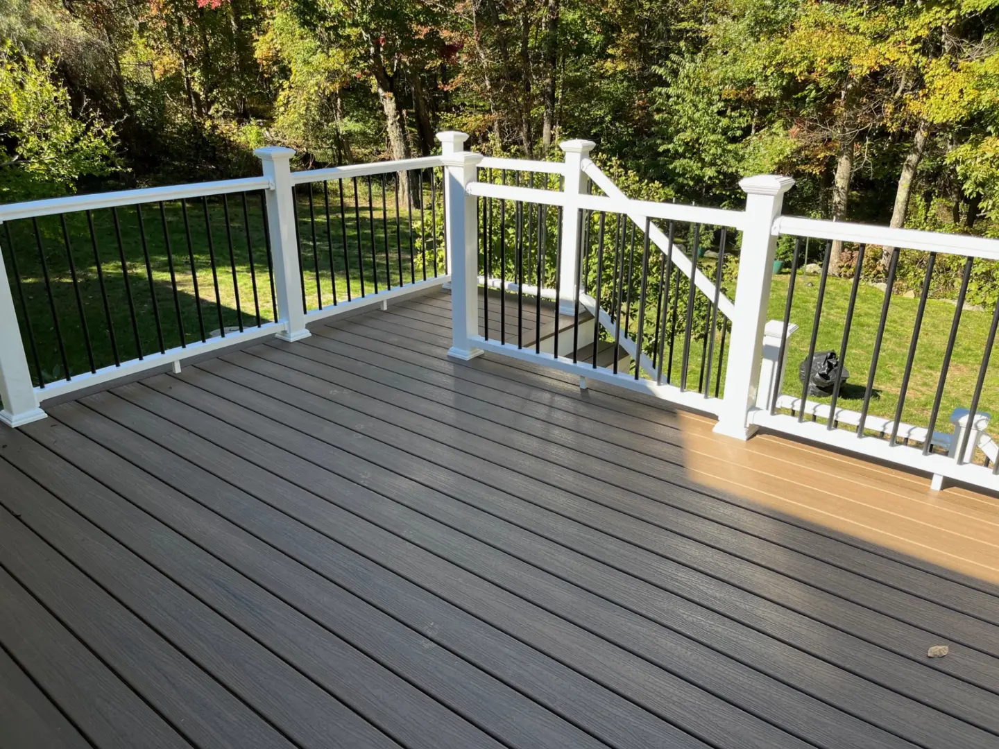 Wooden deck with white and black railing, overlooks grassy yard with trees in background.