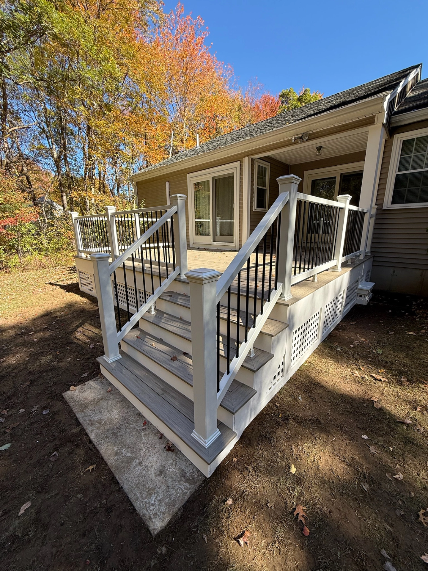 Outdoor deck with white railings and black balusters, leading to a single-story house amidst autumn trees.
