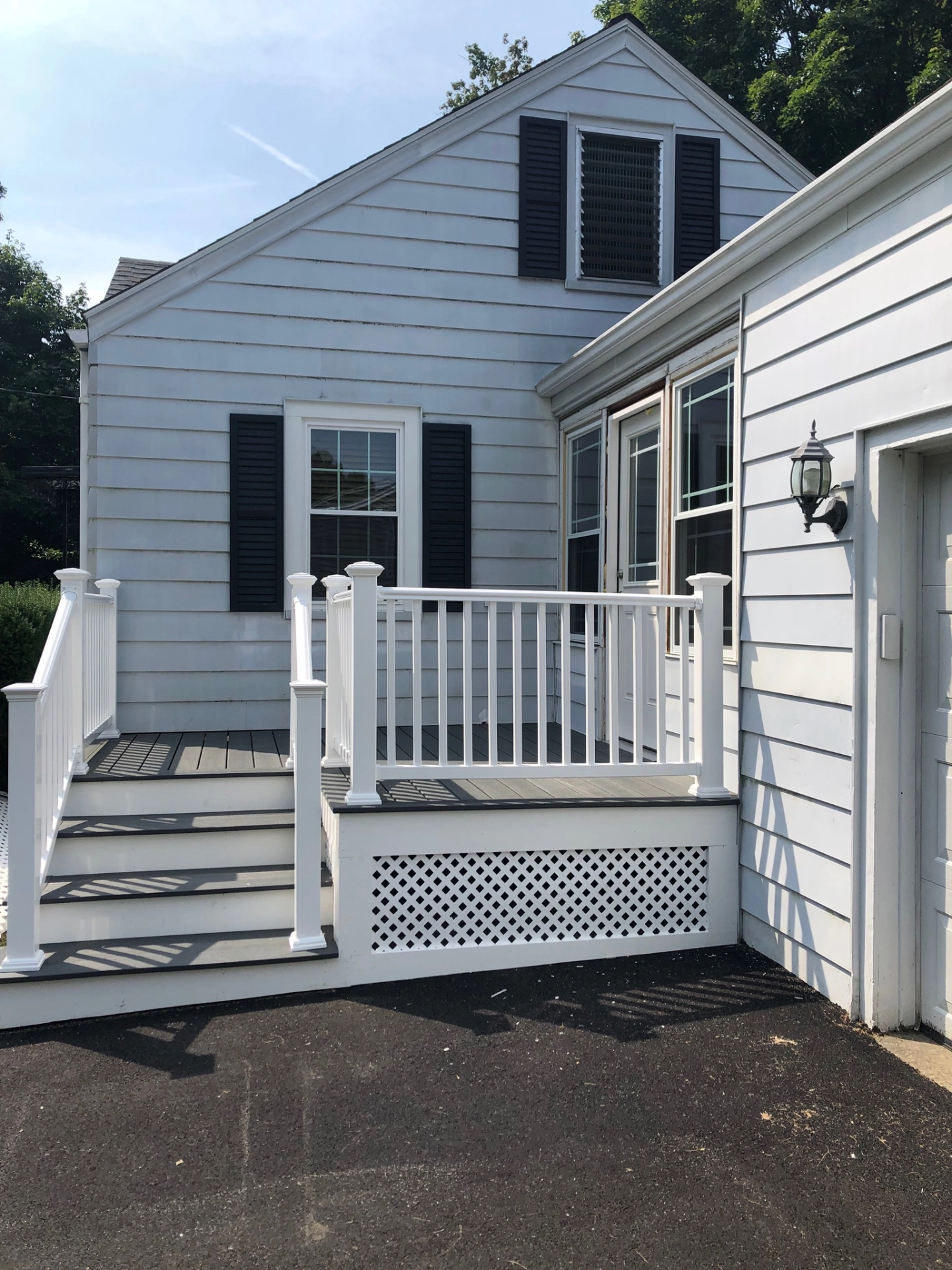White house with black shutters, small porch with white railing and steps, exterior light fixture beside garage door.