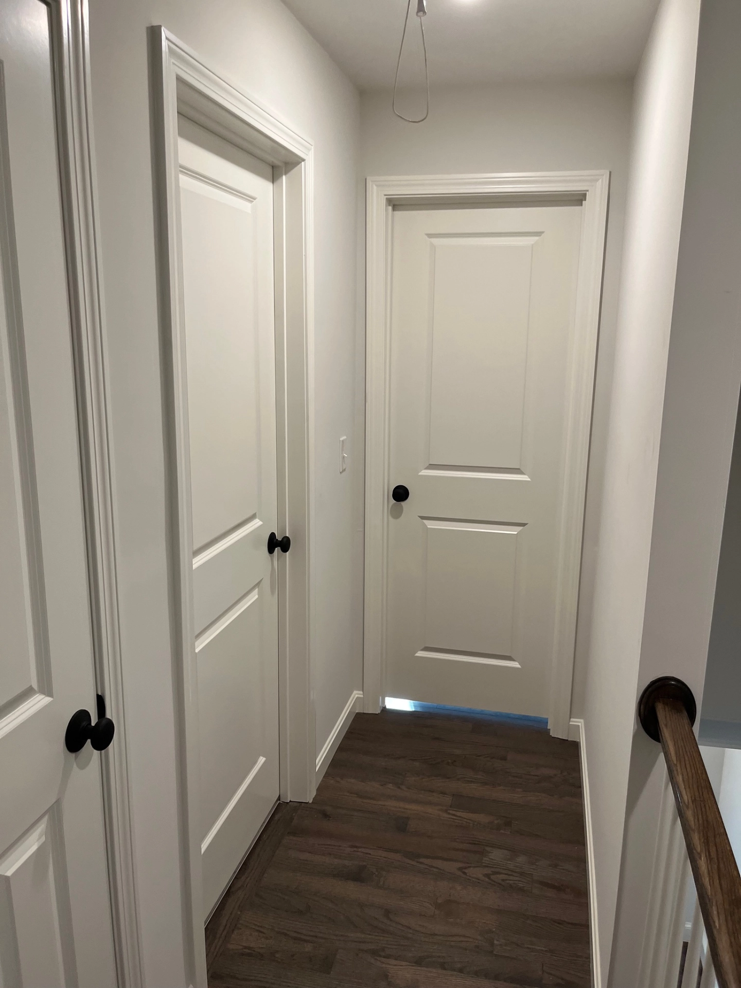 hallway-with-three-white-doors-dark-wood-floor-black-doorknobs-and-a-partially-visible-staircase-railing-in-needham-ma